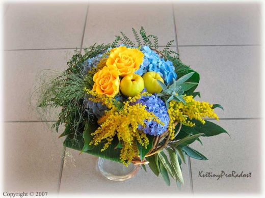 Kulatá kytice ze žlutých růží Sphinx, modré hortensie, solidaga doplněné plody gdouloně.
