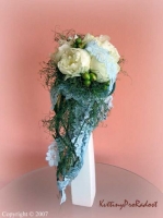 Převislá kytice bílých pivoněk, zdobená modrou krajkou, evokující staré, dobré časy.
