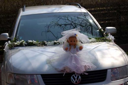 Květinová girlanda s panenkou na kapotě automobilu.